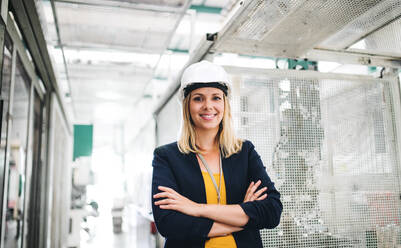 A portrait of a young industrial woman engineer standing in a factory, arms crossed. - HPIF29531