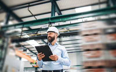 A portrait of a mature industrial man engineer with clipboard standing in a factory. Copy space. - HPIF29533