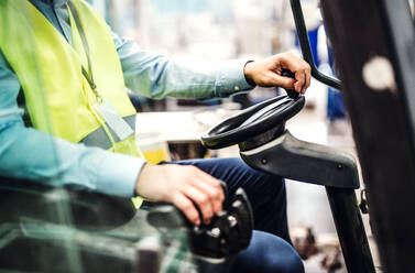 Unrecognizable industrial man engineer or driver sitting in a forklift in a factory. - HPIF29536