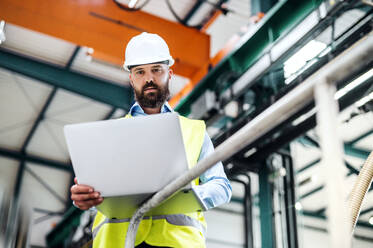 Porträt eines reifen Industrieingenieurs mit Laptop in einer Fabrik, bei der Arbeit. - HPIF29541