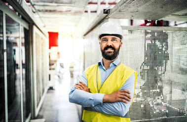 A portrait of a happy industrial man engineer in a factory, arms crossed. - HPIF29547