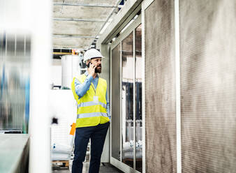 Ein Porträt eines reifen Industrieingenieurs mit Smartphone in einer Fabrik, der einen Anruf tätigt. - HPIF29549