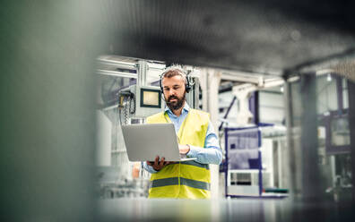 Porträt eines reifen Industrieingenieurs mit Headset und Laptop in einer Fabrik, bei der Arbeit. - HPIF29553