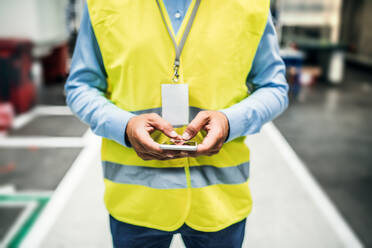 Ein nicht erkennbarer Industrieingenieur mit Namensschild in einer Fabrik, der ein Smartphone benutzt. Raum kopieren. - HPIF29555