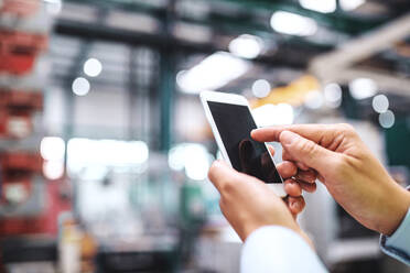 Close-up of female hands in a factory using smartphone. Copy space. - HPIF29556