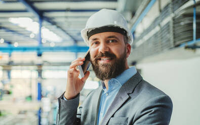 Ein Porträt eines reifen Industrieingenieurs mit Smartphone in einer Fabrik, der einen Anruf tätigt. - HPIF29562