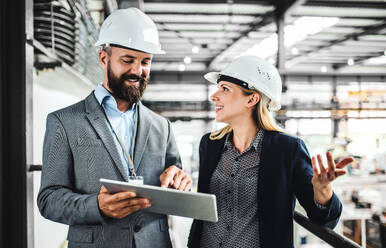 A portrait of a mature industrial man and woman engineer with tablet in a factory, working. - HPIF29568