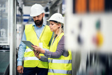 Ein Porträt eines reifen Industriellen und einer Ingenieurin mit Tablet in einer Fabrik, die sich unterhalten. - HPIF29580