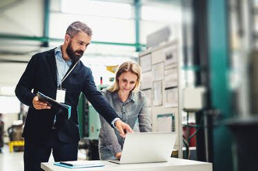 A portrait of a serious mature industrial man and woman engineer with laptop in a factory, working. - HPIF29592