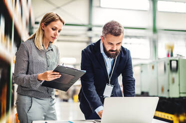 Ein Porträt eines ernsten, reifen Industriemannes und einer Ingenieurin mit Laptop in einer Fabrik bei der Arbeit. - HPIF29594