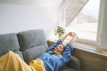 Smiling woman stretching on sofa at home - NDEF00626
