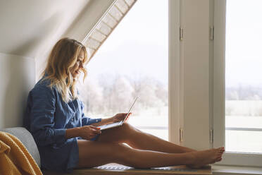 Woman using laptop sitting near attic window at home - NDEF00627