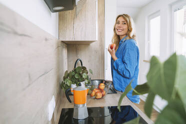 Smiling woman holding apple in kitchen at home - NDEF00631