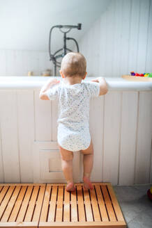 Ein Kleinkind, das im heimischen Badezimmer an der Badewanne steht, Rückansicht. - HPIF29625