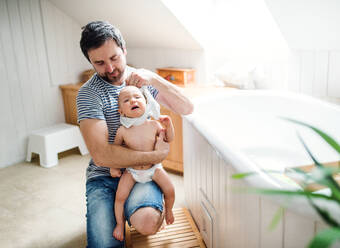 Vater mit einem Kleinkind zu Hause, das sich auf ein Bad vorbereitet. Vaterschaftsurlaub. - HPIF29627