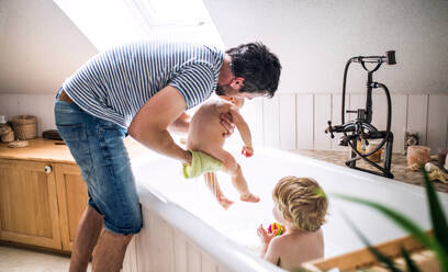 Vater wäscht zwei Kleinkinder in der Badewanne im heimischen Badezimmer. Vaterschaftsurlaub. - HPIF29632