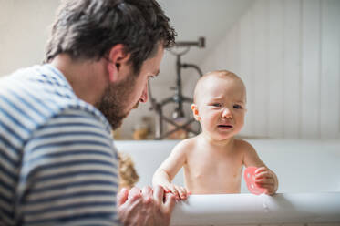 Vater wäscht zwei Kleinkinder in der Badewanne im heimischen Badezimmer. Vaterschaftsurlaub. - HPIF29633