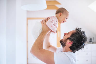 Father holding up a toddler girl in bedroom at home, having fun. Paternity leave. - HPIF29649