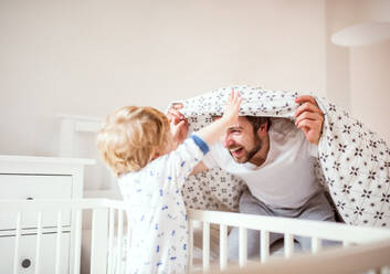 Vater mit einem kleinen Jungen, der sich im Schlafzimmer zu Hause vor dem Schlafengehen amüsiert. Vaterschaftsurlaub. - HPIF29653