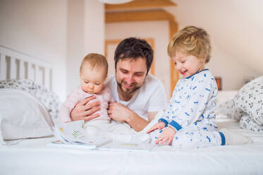 Handsome father with toddler children in bedroom at home, reading stories at bedtime. Paternity leave. - HPIF29660