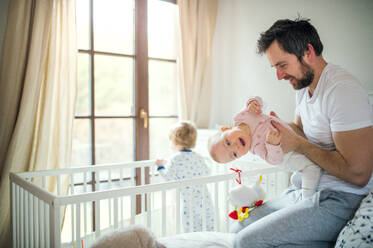 Ein reifer Vater mit Kleinkindern im Schlafzimmer zu Hause zur Schlafenszeit. Vaterschaftsurlaub. Ein Mann hält ein kleines Mädchen, ein Junge steht in einem Kinderbett. - HPIF29665