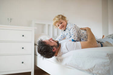 Mature father with a toddler boy having fun in bedroom at home at bedtime. Paternity leave. - HPIF29669