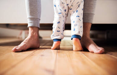 Beine eines nicht erkennbaren Vaters und eines kleinen Jungen, die im heimischen Schlafzimmer auf dem Boden stehen. Vaterschaftsurlaub. Raum kopieren. - HPIF29670