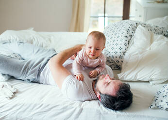 Father with an unhappy toddler girl on bed at home at bedtime. Paternity leave. - HPIF29678