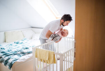 Mature father putting a sleeping toddler girl into a cot at home. Paternity leave. - HPIF29682