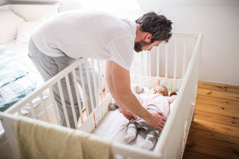 Ein erwachsener Vater legt ein schlafendes Kleinkind zu Hause in ein Kinderbett. Vaterschaftsurlaub. - HPIF29683