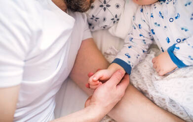 Unrecognizable father holding hand of a sleeping toddler boy lying in bed at home. Paternity leave. - HPIF29685