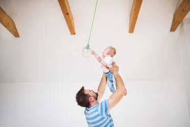 Young father holding a baby son in the air at home. A small boy touching ceiling light. - HPIF29693