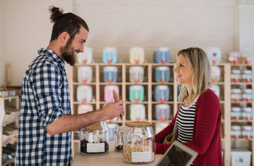 Ein junger, gut aussehender Verkäufer bedient eine Kundin in einem Zero-Waste-Shop. - HPIF29722