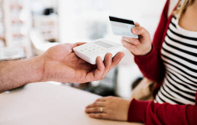 Ein Mittelteil eines Kunden und eines Verkäufers, die in einem Geschäft mit einer Kreditkarte drahtlos oder kontaktlos bezahlen. - HPIF29726