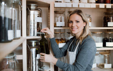 Eine junge Verkäuferin in einem Zero-Waste-Shop füllt eine Flasche mit Olivenöl. - HPIF29761