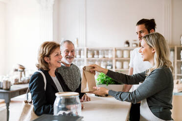 Ein älteres Ehepaar kauft Lebensmittel in einem Zero-Waste-Laden, während die Verkäuferinnen sie bedienen. - HPIF29764