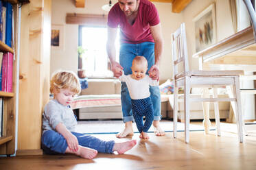 Vater mit zwei Kleinkindern zu Hause, erste Schritte, Vaterschaftsurlaub. - HPIF29781