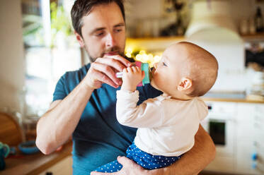 Ein Vater mit einer kleinen Tochter zu Hause. Ein süßes Mädchen, das Wasser aus der Flasche trinkt. Vaterschaftsurlaub. - HPIF29813