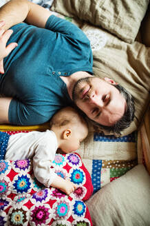 Vater mit einem kleinen Mädchen zu Hause, das auf dem Sofa schläft. Vaterschaftsurlaub. Ansicht von oben. - HPIF29819