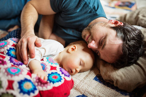 Vater mit einem kleinen Mädchen zu Hause, das auf dem Sofa schläft. Vaterschaftsurlaub. - HPIF29820