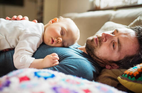 Vater mit einem kleinen Mädchen zu Hause, das auf dem Sofa schläft, Vaterschaftsurlaub, Nahaufnahme. - HPIF29822