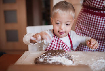 Ein behindertes Kind mit Down-Syndrom und seine unerkennbare Mutter mit karierten Schürzen backen in einer Küche. - HPIF29828