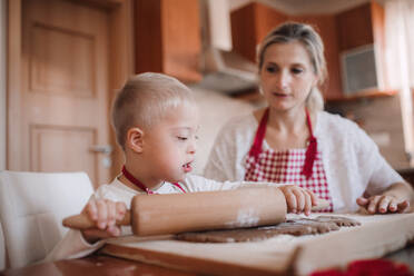A handicapped down syndrome child and his mother with checked aprons indoors baking in a kitchen. - HPIF29832