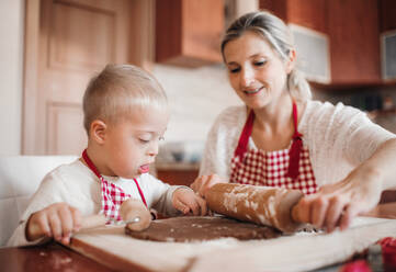 Ein behindertes Kind mit Down-Syndrom und seine Mutter mit karierten Schürzen beim Backen in einer Küche. - HPIF29833