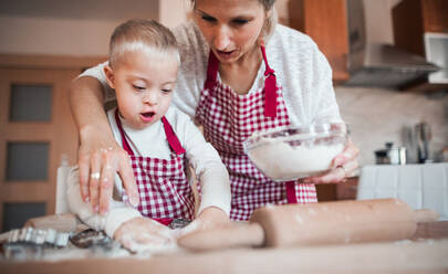 Ein glückliches behindertes Kind mit Down-Syndrom und seine Mutter backen in einer Küche. - HPIF29843