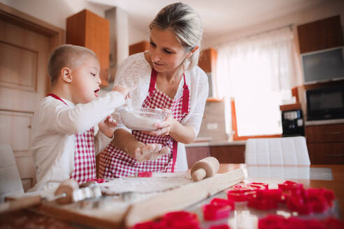 Ein behindertes Kind mit Down-Syndrom und seine Mutter mit karierten Schürzen beim Backen in einer Küche. - HPIF29844