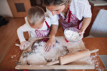 Ein behindertes Kind mit Down-Syndrom und seine Mutter mit karierten Schürzen beim Backen in einer Küche, von oben gesehen. - HPIF29845