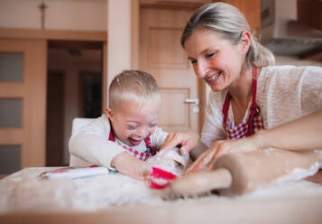 Ein glückliches behindertes Kind mit Down-Syndrom und seine Mutter backen in einer Küche. - HPIF29849