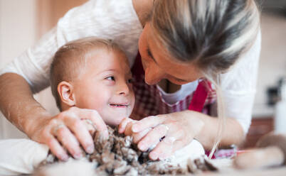 Ein glückliches behindertes Kind mit Down-Syndrom und seine Mutter backen in einer Küche, Nahaufnahme. - HPIF29851