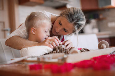 Ein glückliches behindertes Kind mit Down-Syndrom und seine Mutter backen in einer Küche. - HPIF29853